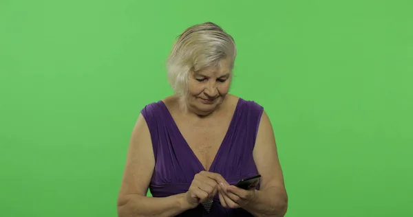 Een oudere vrouw werkt op een smartphone. Oude grootmoeder glimlacht. Chroma Key — Stockfoto