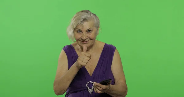 Starsza kobieta pracuje na smartfonie. Stara babcia uśmiecha się. Klucz chrominancji — Zdjęcie stockowe