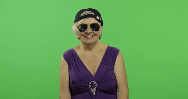 Vieille et heureuse grand-mère en lunettes de soleil et casquette. Chroma arrière-plan clé — Photo