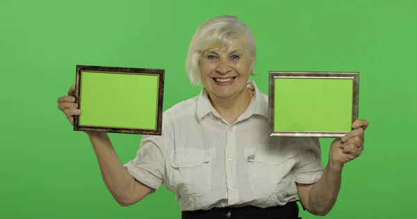 Starsza kobieta trzyma dwie klatki z zielonym obrazem. Babcia. Klucz chrominancji — Zdjęcie stockowe