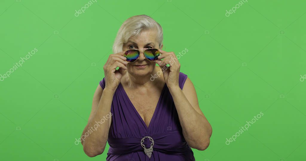 An elderly woman in sunglasses smiles. Old pretty happy grandmother in a purple dress. Place for your logo or text. Chroma key. Green screen background