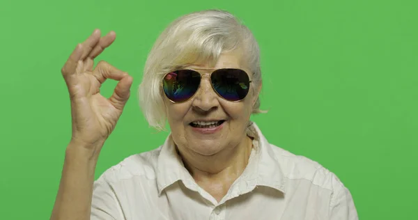 Starsza kobieta w okularach pokazuje OK gest i uśmiechy. Klucz chrominancji — Zdjęcie stockowe