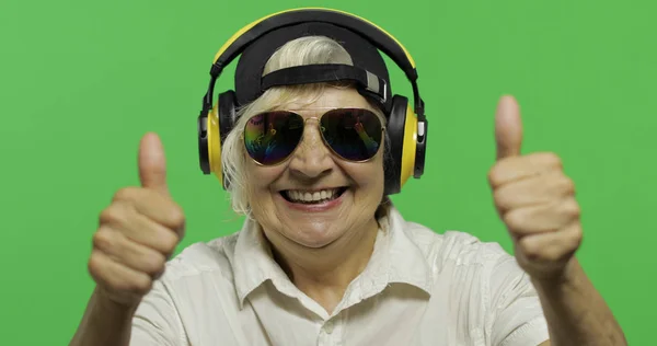 Elderly woman listens to music in headphones. Thumb up. Grandmother. Chroma key