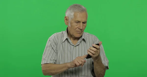 Homem sênior trabalha em um smartphone. Bonito homem velho no fundo da chave chroma — Fotografia de Stock