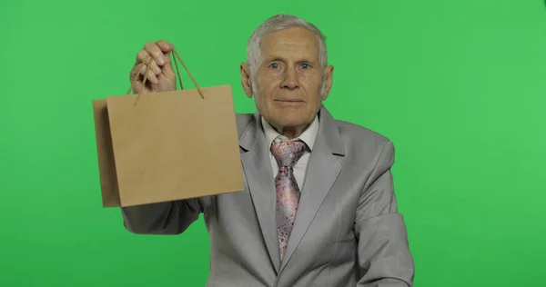 Oudere man met boodschappentas. Kijkt naar de camera en strekt het geschenk uit — Stockfoto
