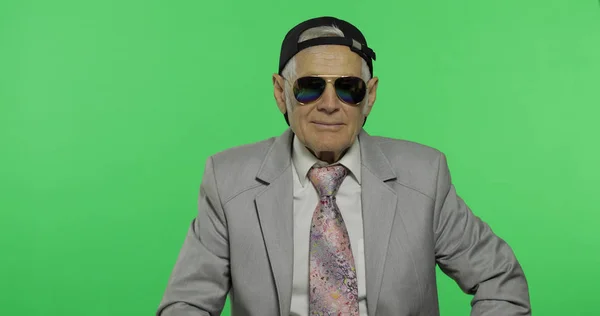 Divertido hombre de negocios de edad avanzada en gafas de sol y sonrisas gorra. Viejo guiña un ojo — Foto de Stock