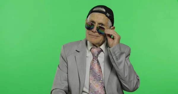 Funny elderly businessman in sunglasses and cap smiles. Old man winks