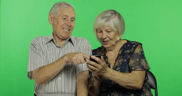 Üst düzey yaşlı adam ve kadın birlikte oturan ve smartphone üzerinde çalışıyor. Chroma anahtarı