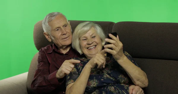 Starszy mężczyzna i kobieta siedzący razem na kanapie i pracujący na smartfonie — Zdjęcie stockowe