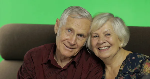 Мужчина и женщина старшего возраста сидят вместе на диване и улыбаются. Ключ хрома — стоковое фото