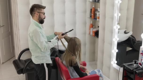 Peluquería profesional que trabaja con el cabello modelo. Enderezamiento de hierro corrugado — Vídeo de stock