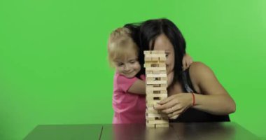 Anne ve kızı jenga oynar. Çocuk kuleden ahşap bloklar çeker