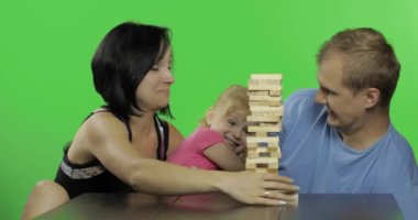 Anne, baba ve kızı jenga çalıyor. Kuleden tahta bloklar çekiyor.