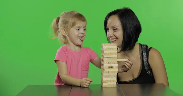 母と娘はジェンガを演じます。子供は塔から木製のブロックを引っ張ります — ストック写真