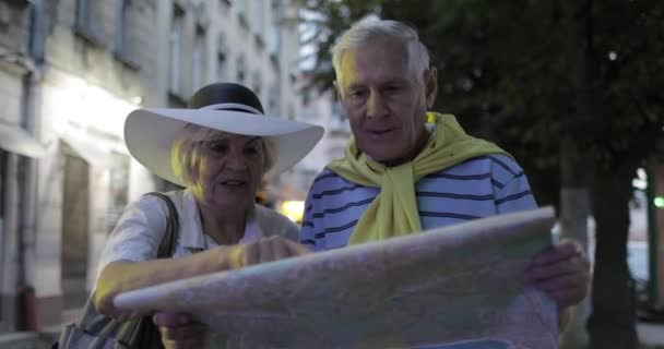 Старшие туристы мужского и женского пола, стоящие с картой в руках, ищут маршрут — стоковое видео