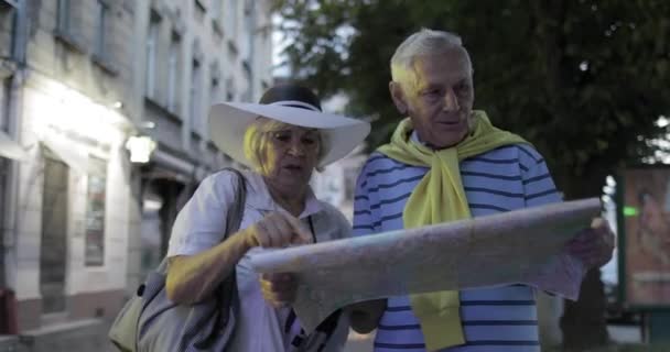 Senior male and female tourists standing with a map in hands looking for route — Stock Video