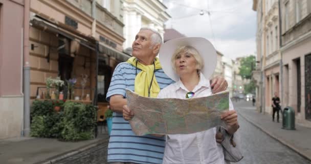 Turistas senior masculinos y femeninos de pie con un mapa en las manos buscando ruta — Vídeos de Stock