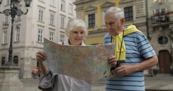 Turistas senior masculinos y femeninos caminando con un mapa en las manos buscando ruta — Vídeo de stock
