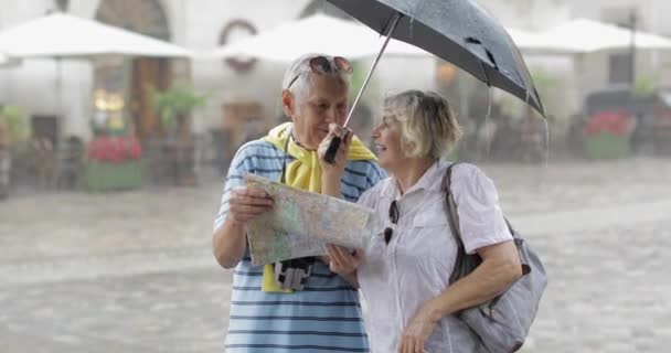 Starsi turyści w deszczowej pogodzie stoją i szukają trasy na mapie — Wideo stockowe