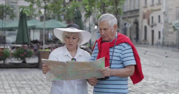 Turistas senior masculinos y femeninos de pie con un mapa en las manos buscando ruta — Vídeos de Stock