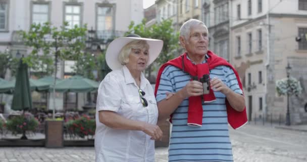 Şehir merkezinde yürüyen ve dürbünle bakan yaşlı erkek ve kadın turistler — Stok video