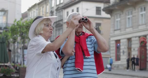 Mayores turistas masculinos y femeninos caminando en el centro de la ciudad y mirando en prismáticos — Vídeos de Stock