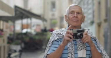 Kıdemli erkek turist şehir keşfetmek ve retro fotoğraf makinesi ile bir fotoğraf yapar