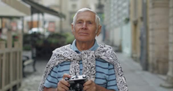 Старший турист осматривает город и делает фото с ретро-фотоаппаратом — стоковое видео