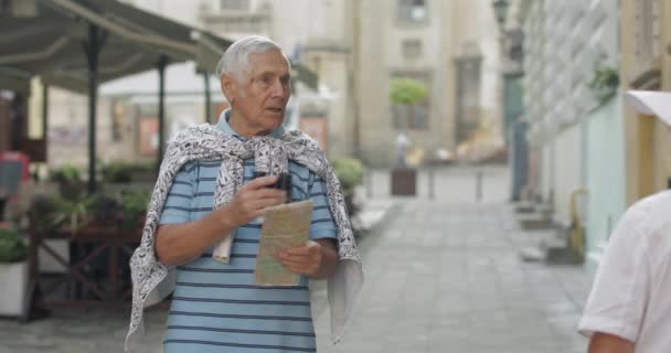 Sénior turista masculino pedindo a mulher para direções na cidade usando um mapa em mãos — Vídeo de Stock