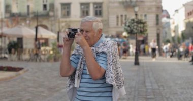 Kıdemli erkek turist şehir keşfetmek ve retro fotoğraf makinesi ile bir fotoğraf yapar