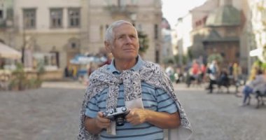 Kıdemli erkek turist şehir keşfetmek ve retro fotoğraf makinesi ile bir fotoğraf yapar
