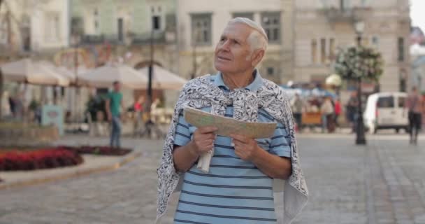 Senior turista masculino explorando la ciudad con un mapa en las manos. Buscando la ruta — Vídeos de Stock