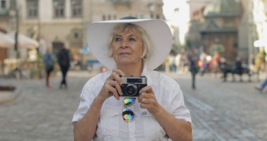 Büyük kadın turist şehir keşfetmek ve retro fotoğraf makinesi ile bir fotoğraf yapar