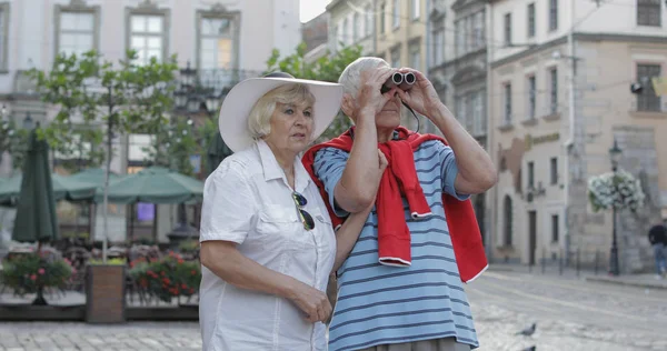 Senior male and female tourists walking in town center and looking in binoculars Stock Image