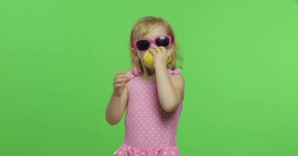 Niño en traje de baño rosa y gafas de sol come una pera verde. Clave de croma — Vídeo de stock