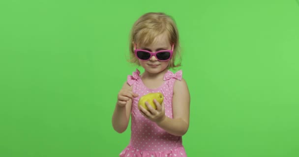 Child in pink swimsuit and sunglasses eats a green pear. Chroma Key — Stock Video