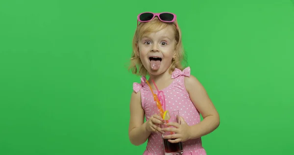 Enfant en maillot de bain rose montrer la langue et tient cocktail de jus avec de la paille à boire — Photo