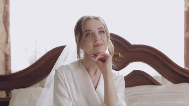 Schöne und reizende Braut in Nachthemd und Schleier auf dem Bett sitzend. Zeitlupe — Stockvideo