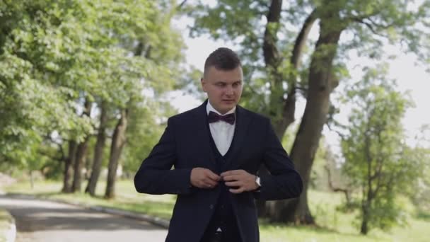 Groom, brunette young man walking in the park and fastens the jacket — Stock Video