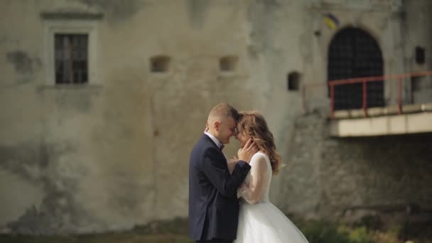 Kaukasiska brudgummen med bruden nära gamla slottsmuren. Bröllopspar. Lyckliga nygifta — Stockvideo