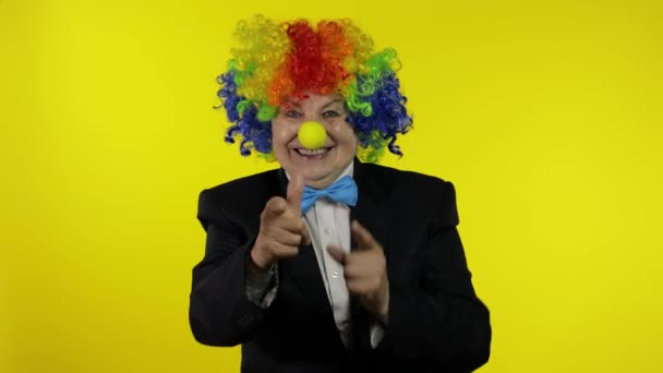 Vecchia clown anziana in parrucca sorridente, sciocca in giro, facendo segni di tiro dalle mani — Video Stock