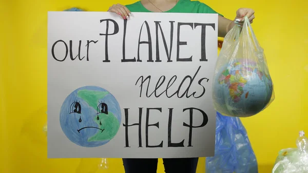 Unrecognizable woman with protesting poster and Earth globe in plastic package. Ecology pollution