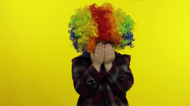 Badut anak kecil dengan wig warna-warni bersembunyi di balik tangannya dan menunjukkan wajah lucu. Halloween — Stok Video