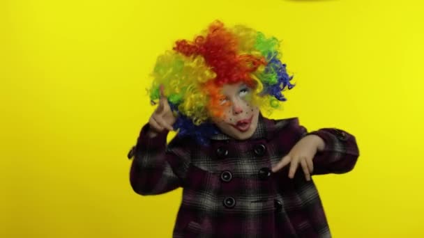 Маленькая девочка-клоун в радужном парике строит глупые рожи. Веселитесь, улыбаетесь, танцуете. Хэллоуин — стоковое видео