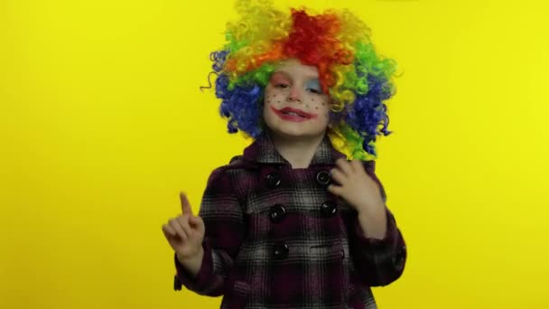 Маленька дівчинка клоун в барвистій перуці робить дурні обличчя. Розважаючись, показує фокуси. Хеллоуїн — стокове відео