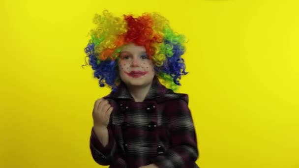 Kleines Kindermädchen Clown in Regenbogenperücke macht dumme Gesichter. Spaß haben, lächeln, tanzen. Halloween — Stockvideo