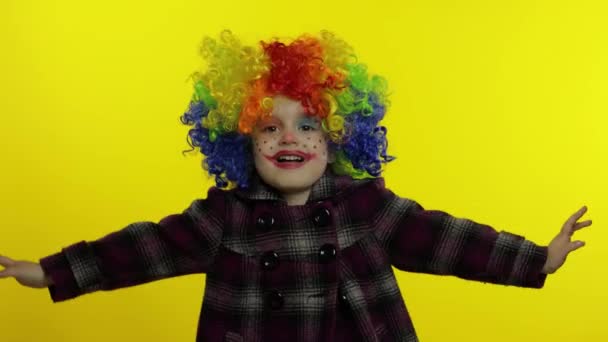 Маленькая девочка-клоун в красочном парике делает глупые лица, веселится, улыбается, танцует. Хэллоуин — стоковое видео