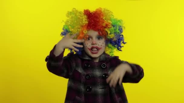 Een kleine clown met een kleurrijke pruik die rare gezichten trekt. Plezier hebben, zingen, dansen. Halloween — Stockvideo