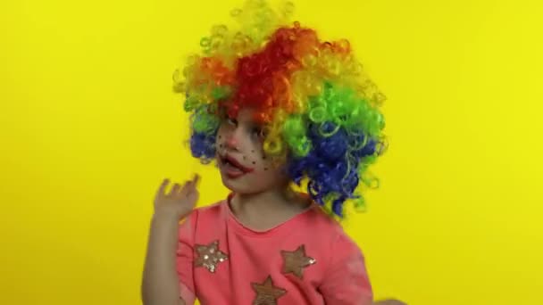 Petite fille clown en perruque arc-en-ciel faisant des visages stupides. Fou, souriant, dansant. Halloween — Video