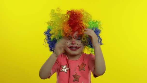 Little child girl clown in colorful wig making silly faces, crying. Halloween. Yellow background — Stock Video